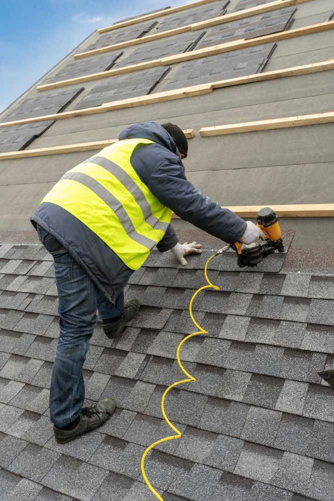 Worker in safety vest using a nail gun to install shingles on a sloped roof