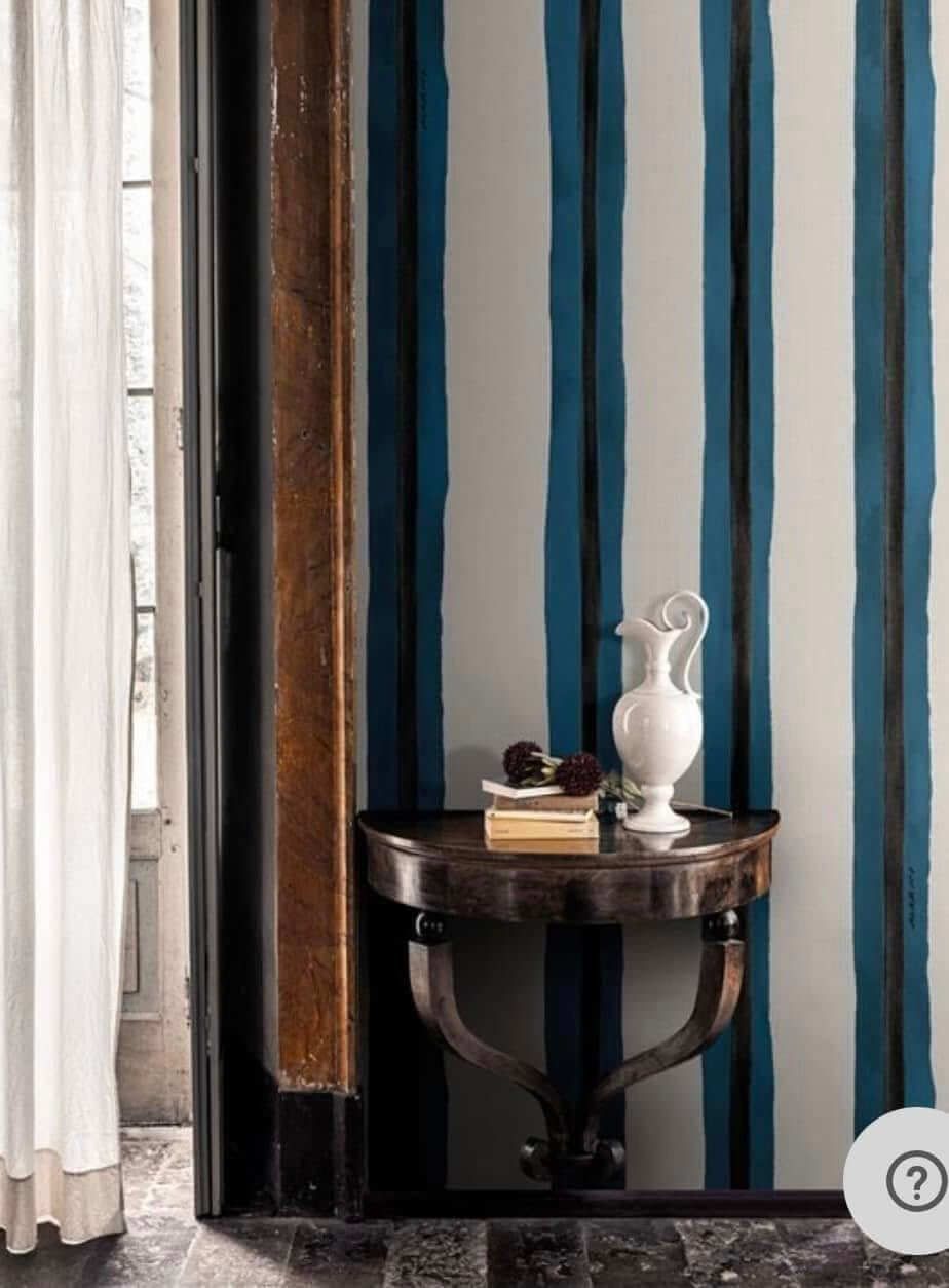 C'è un tavolo con un vaso sopra davanti a una parete a strisce.