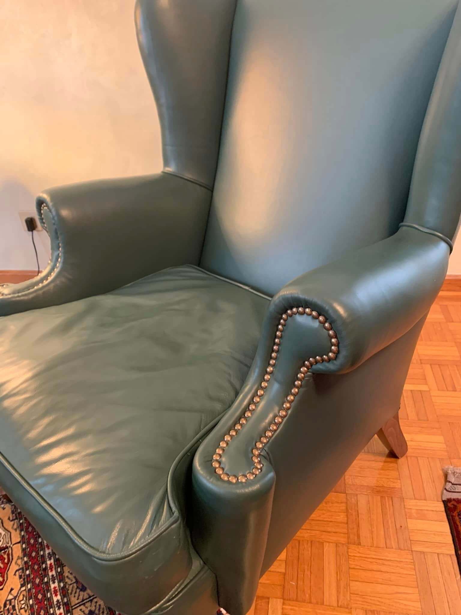 Una sedia in pelle verde è appoggiata su un pavimento in legno.