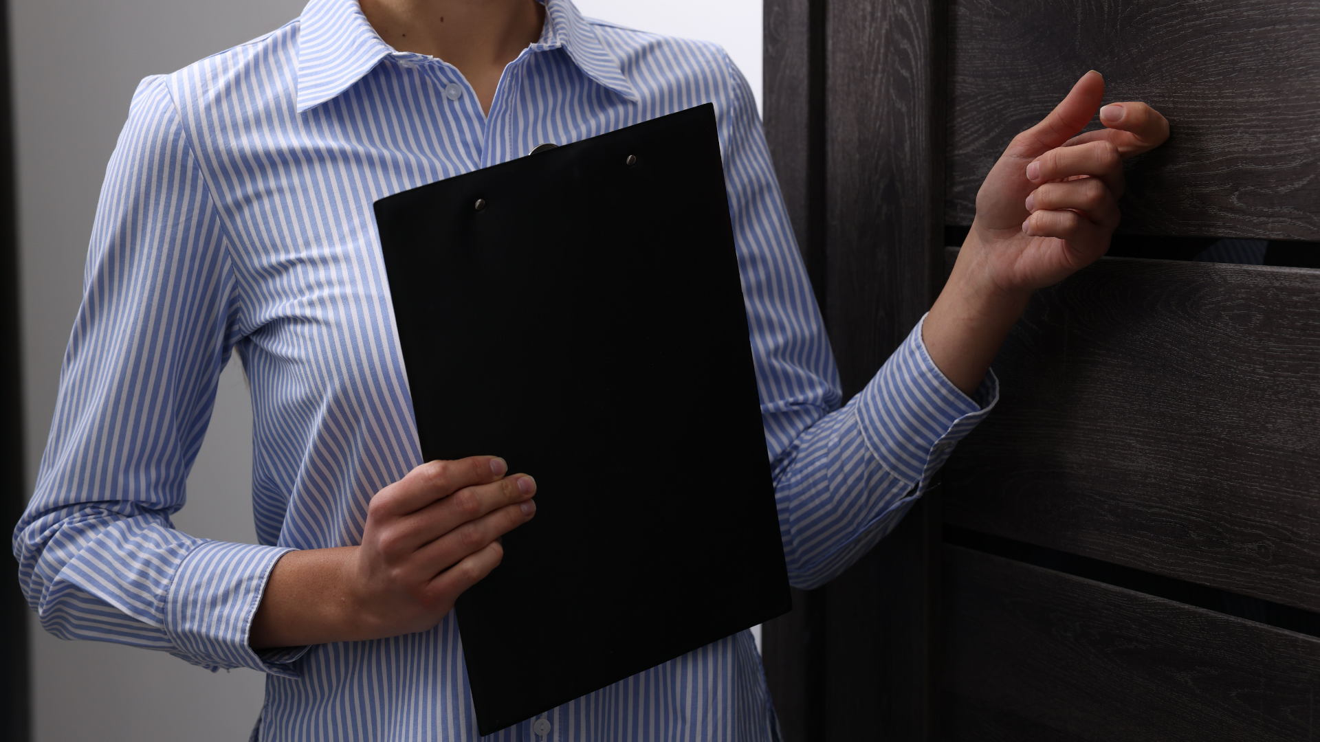 A woman is holding a clipboard and knocking on a door.