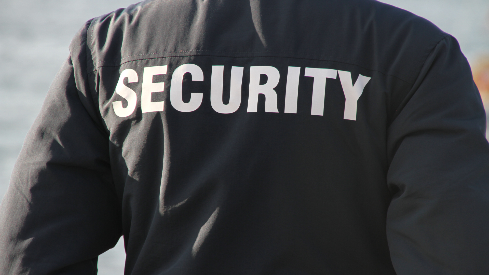 A security guard is wearing a black jacket with the word security on the back.