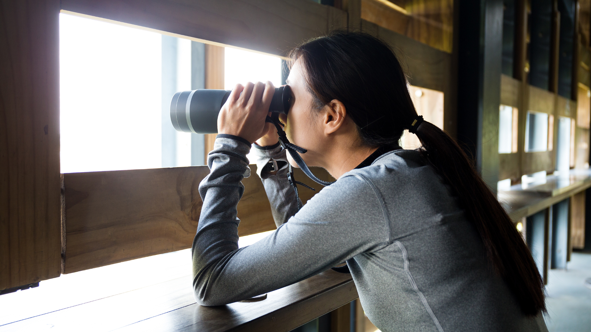 A woman is looking through binoculars out of a window.