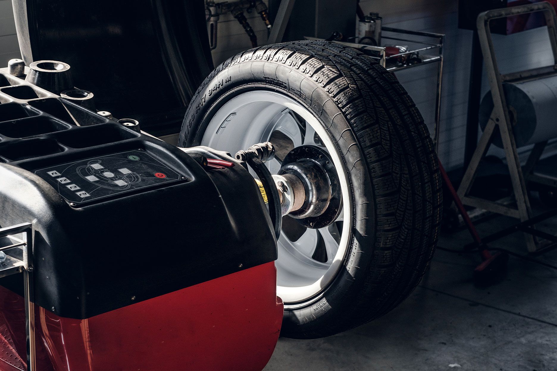 Car tire on a wheel balancer in a dim garage, with a red and black machine in the foreground