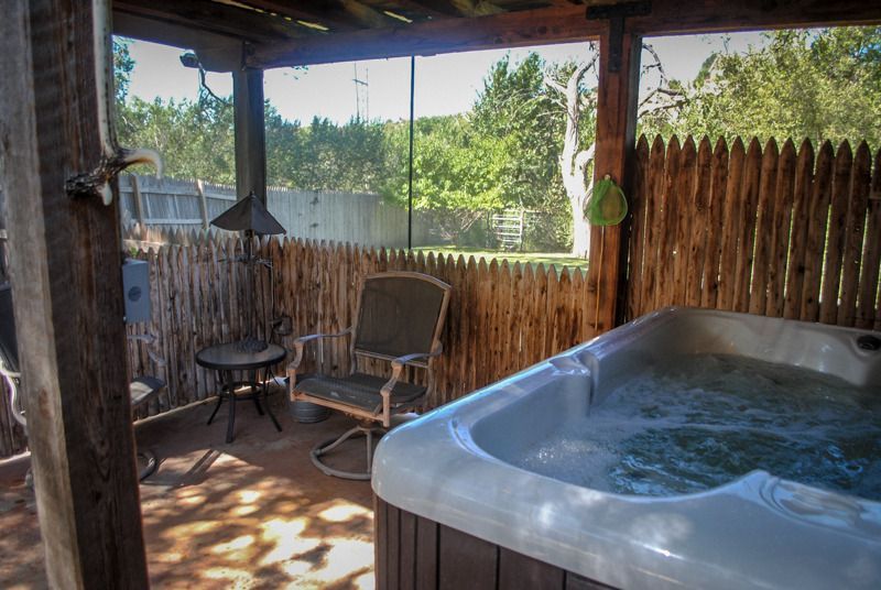 A hot tub is sitting under a wooden fence on a patio.