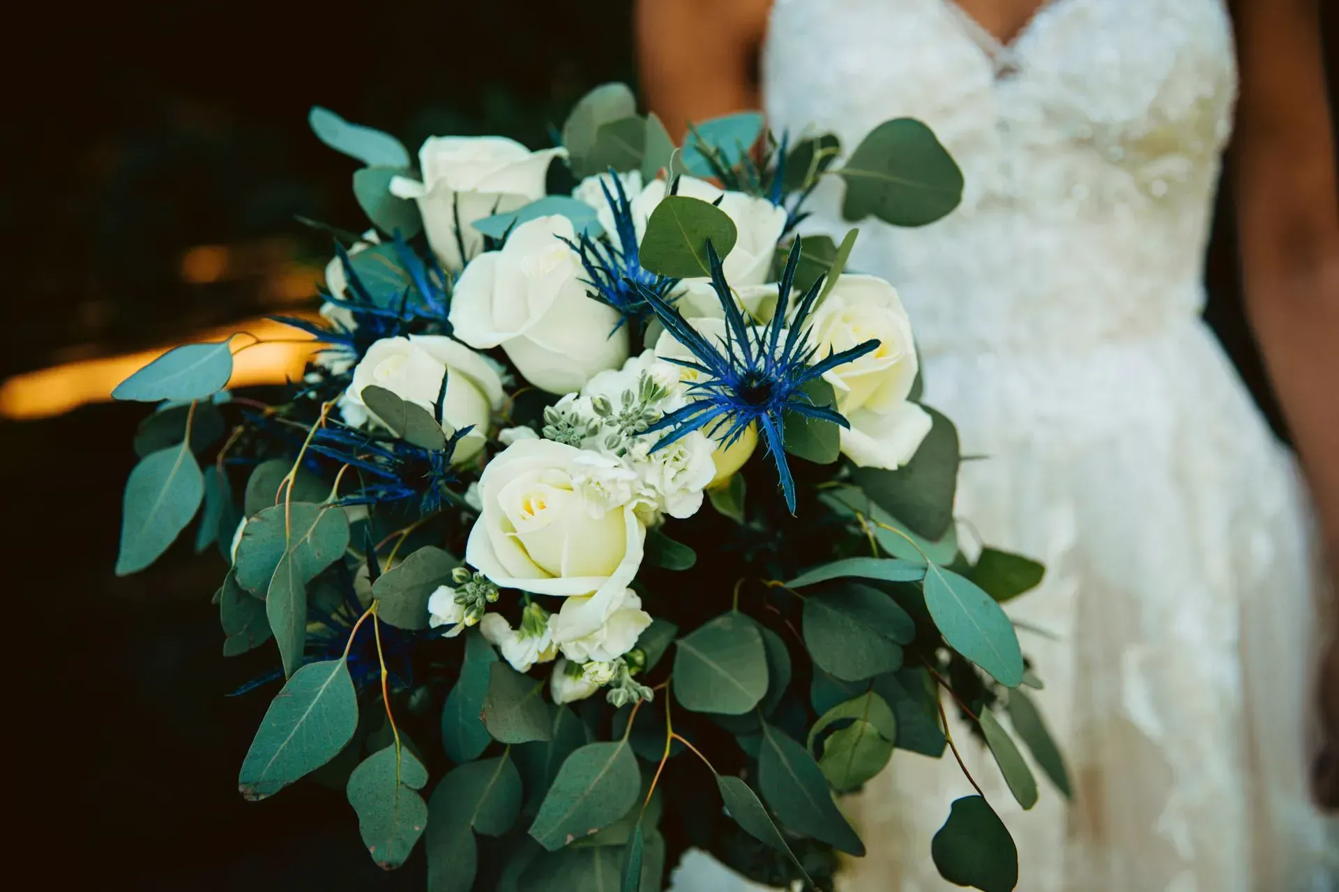 A bride in a white dress is holding a bouquet of white and blue flowers.