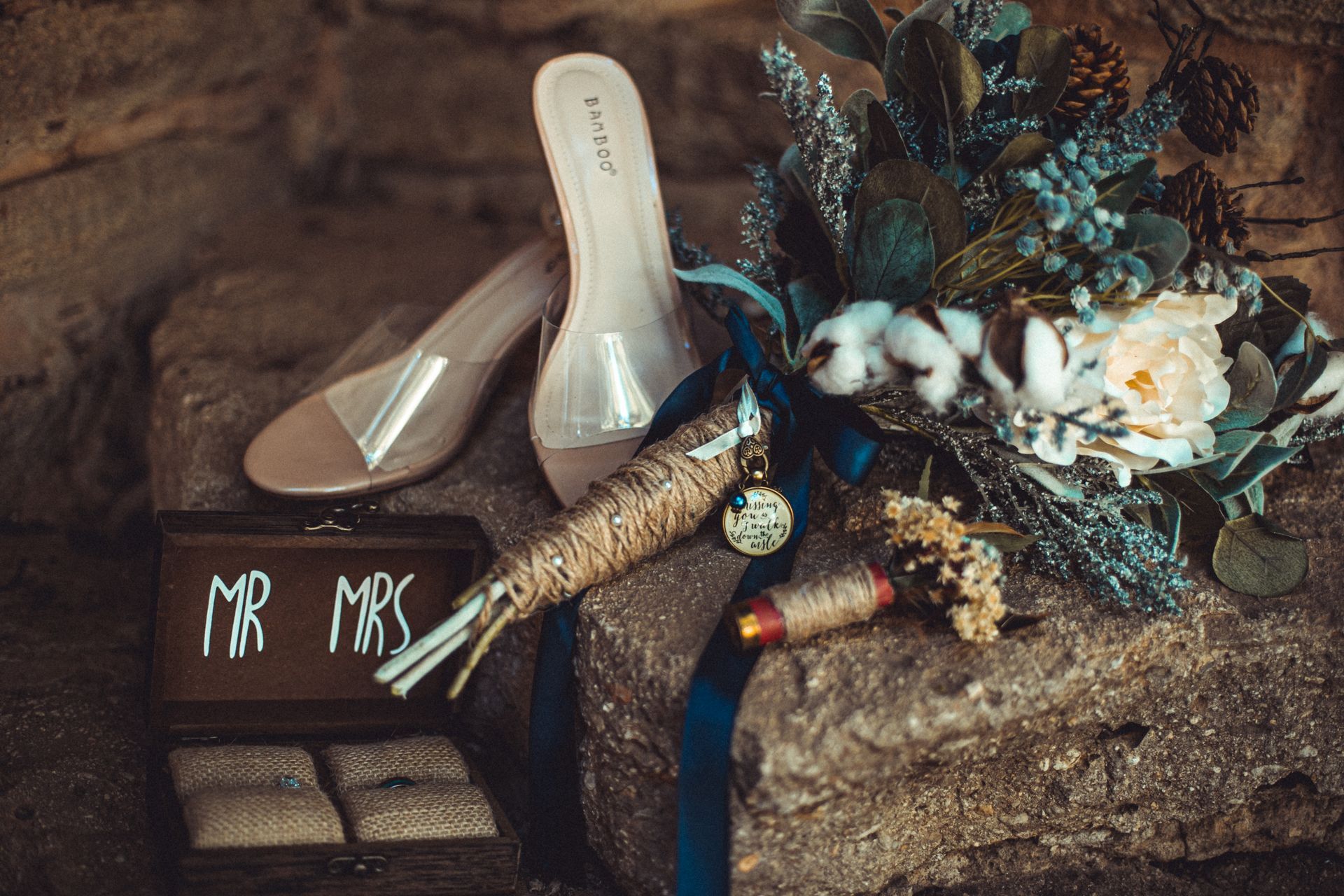 A bouquet of flowers , a pair of shoes , a ring box and a sign on a rock.