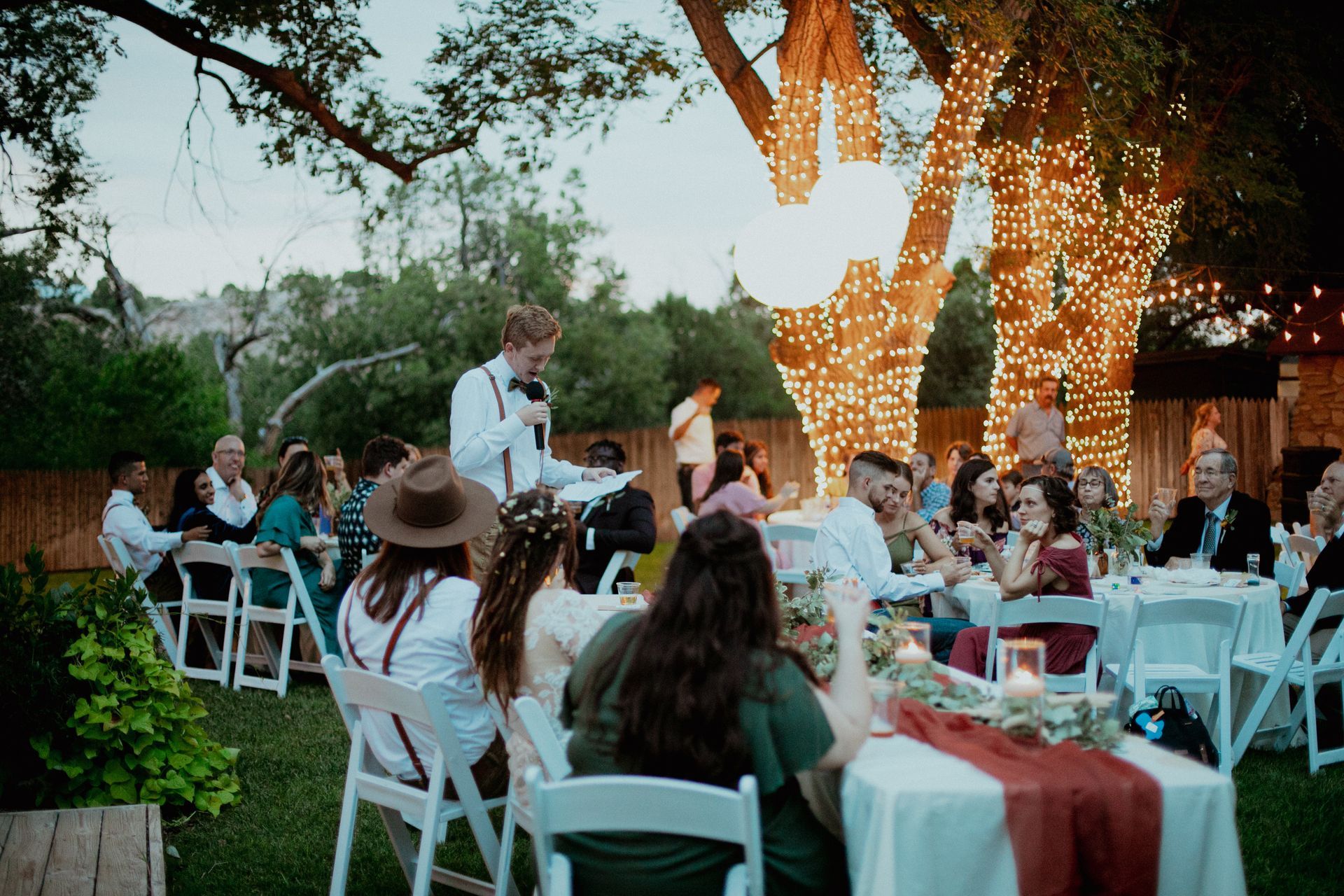 A group of people are sitting at tables outside at a wedding reception.