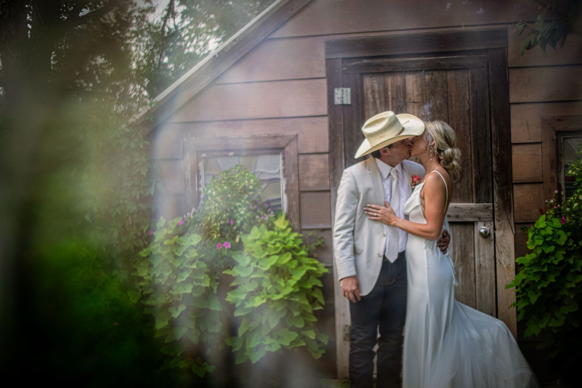 A bride and groom are kissing in front of a wooden building.