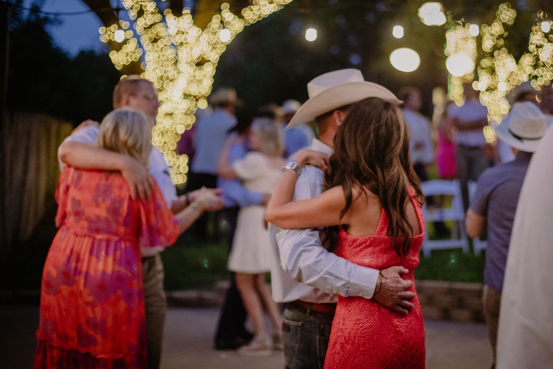A man in a cowboy hat is dancing with a woman in a red dress at a wedding reception.