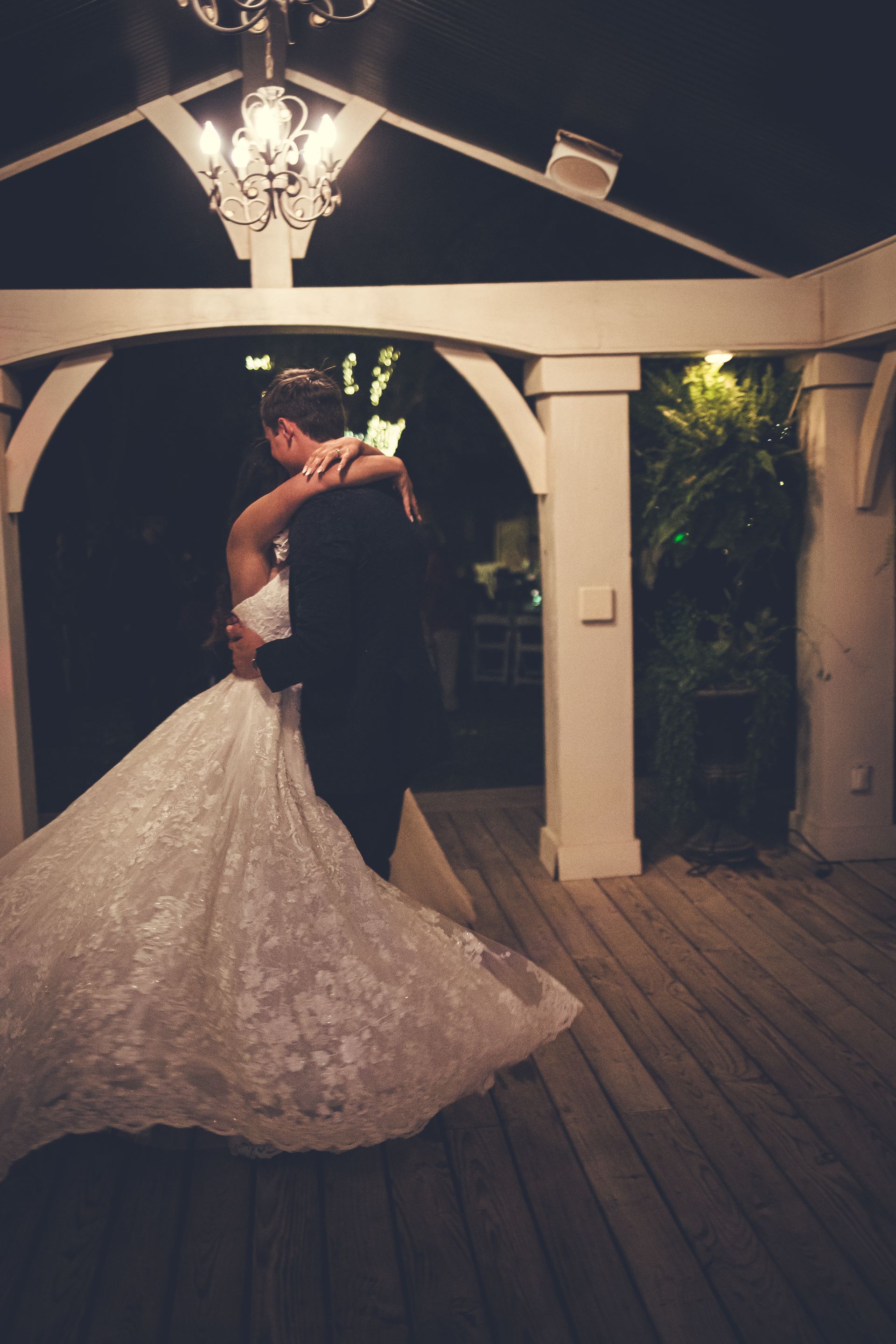 A bride and groom are dancing under a gazebo at night