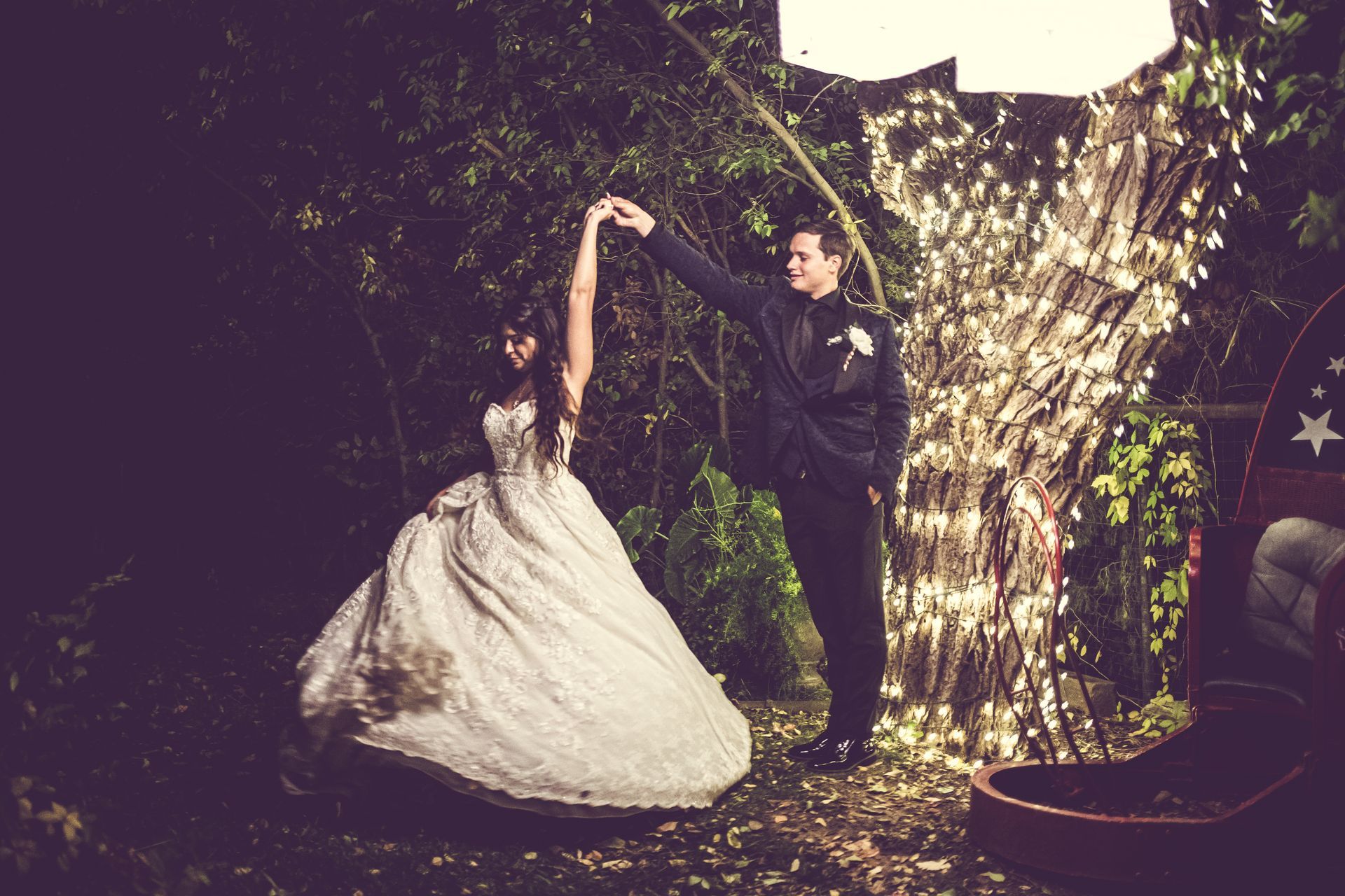 A bride and groom are dancing in the woods at night.