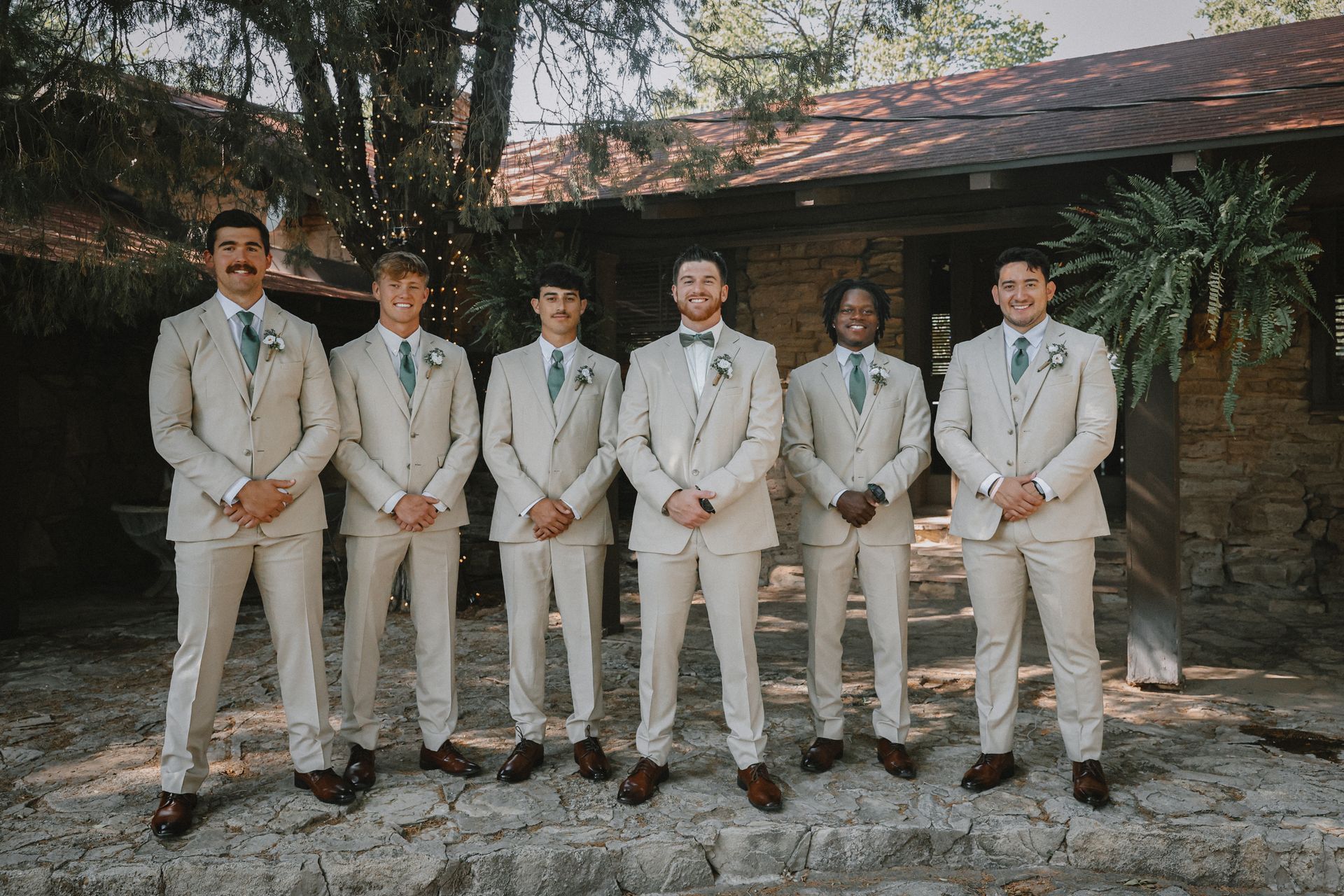 The groom and his groomsmen are posing for a picture in front of a stone building.