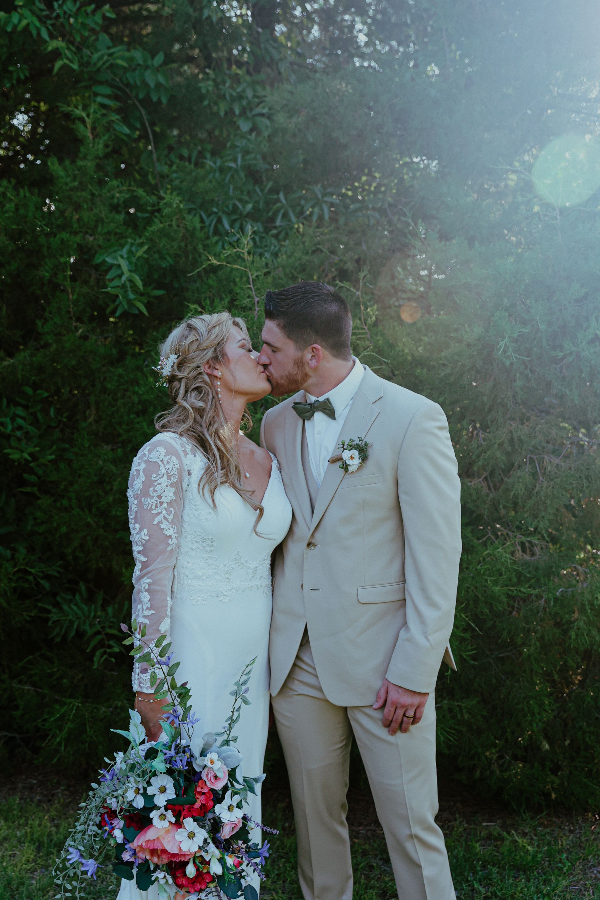A bride and groom are kissing in front of trees.