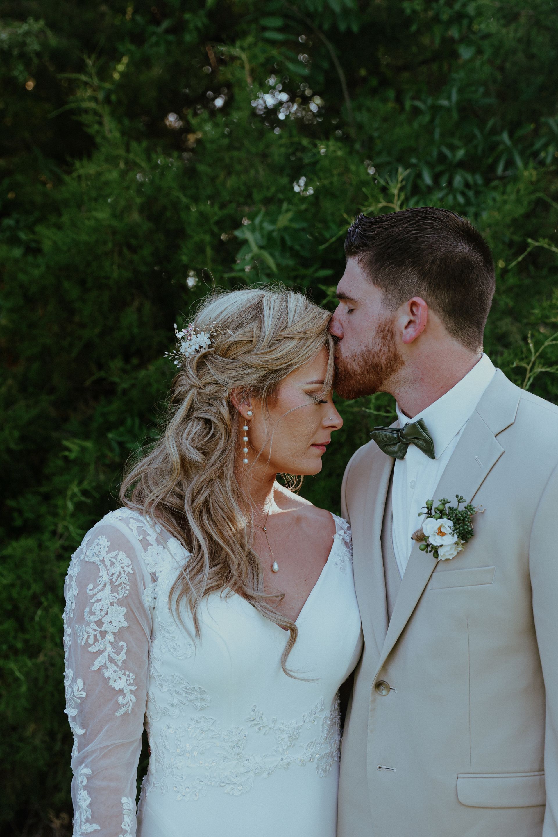 A bride and groom are kissing in front of a tree.
