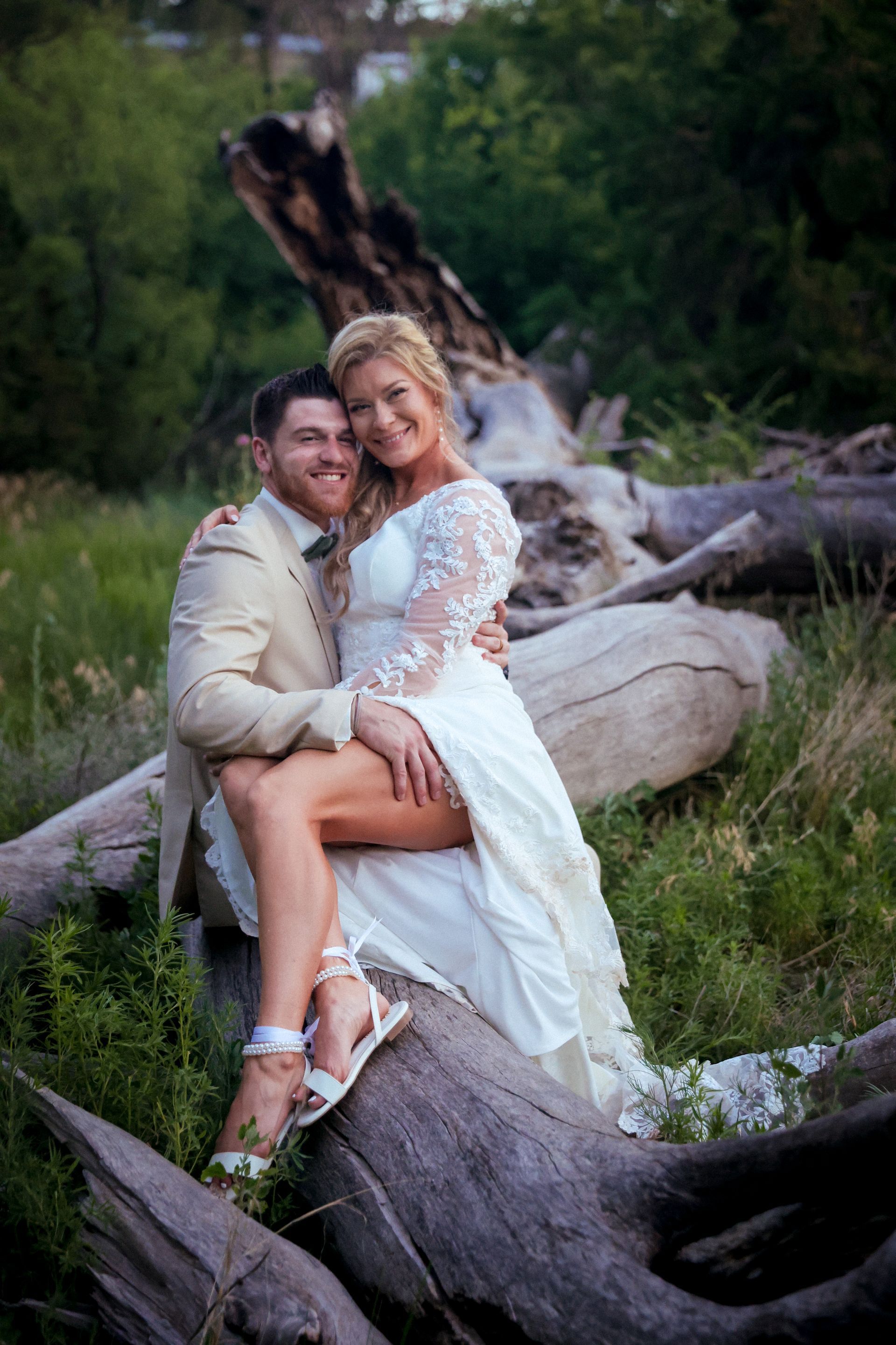 A bride and groom are posing for a picture while sitting on a log.