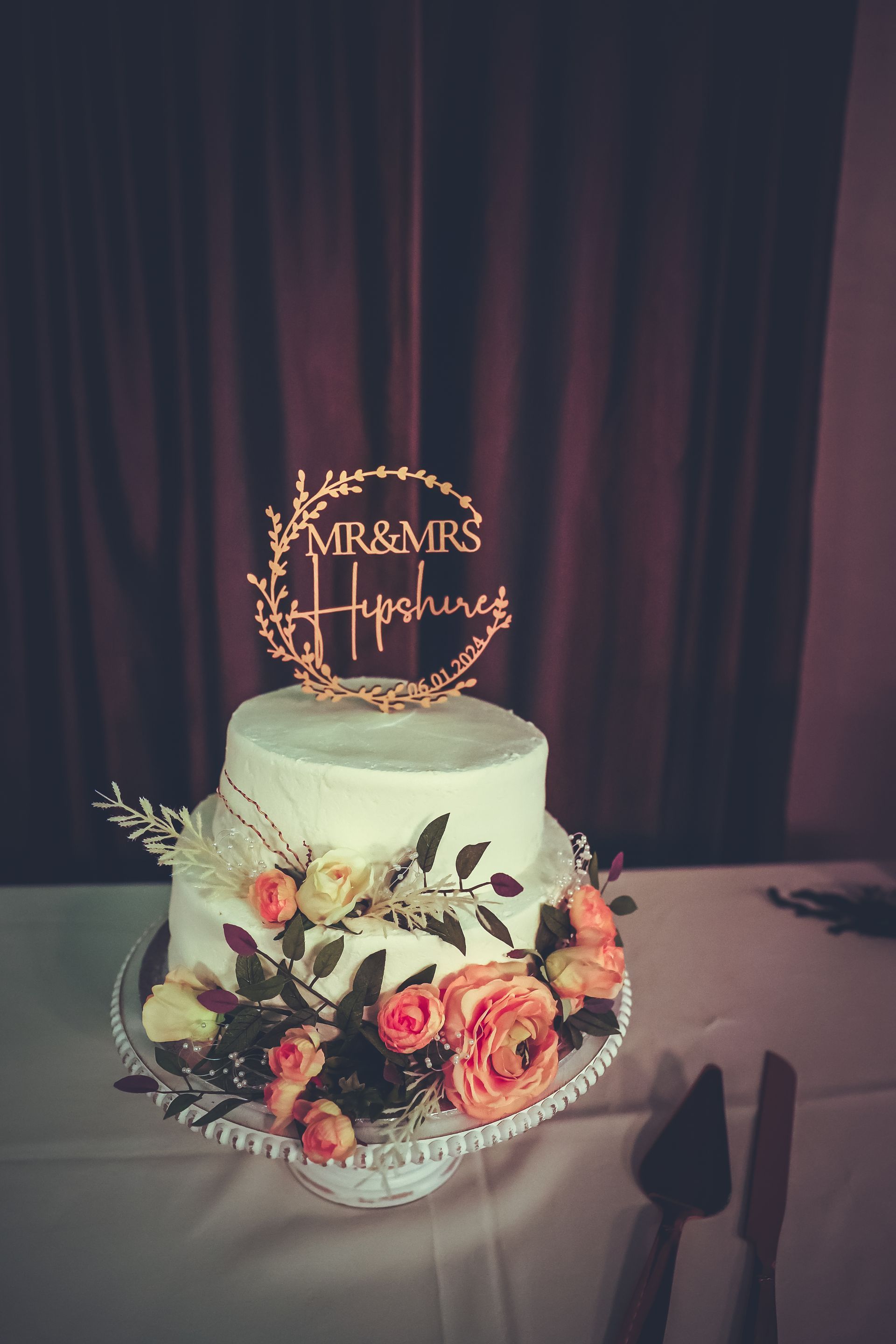A wedding cake with flowers and a cake topper on a table.