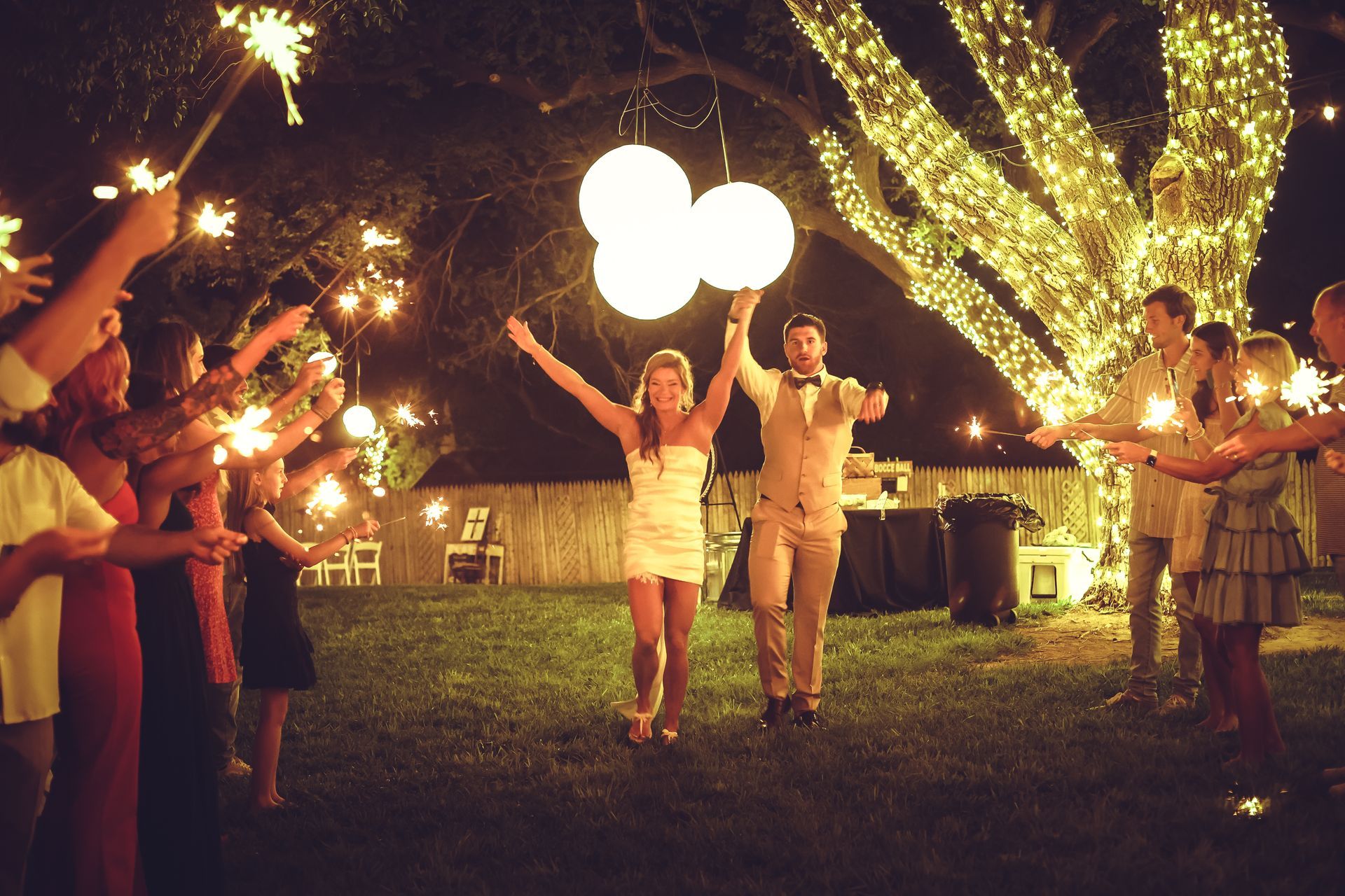 A bride and groom are walking through a crowd of people holding sparklers