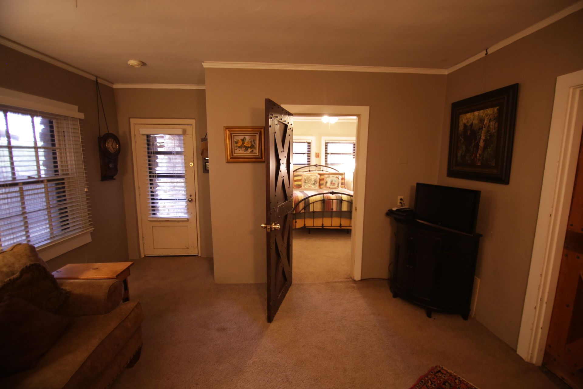 A living room with a couch and a television looking into a bedroom.