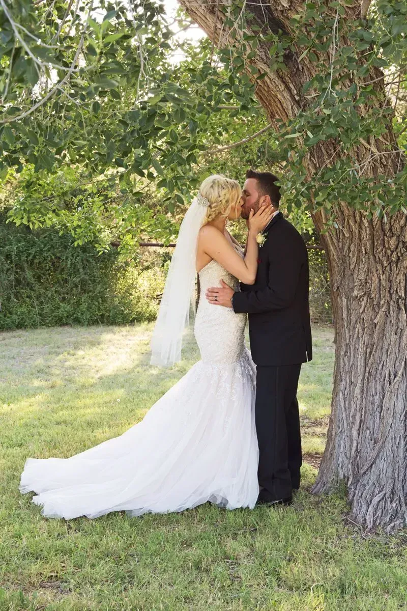 A bride and groom are kissing under a tree.