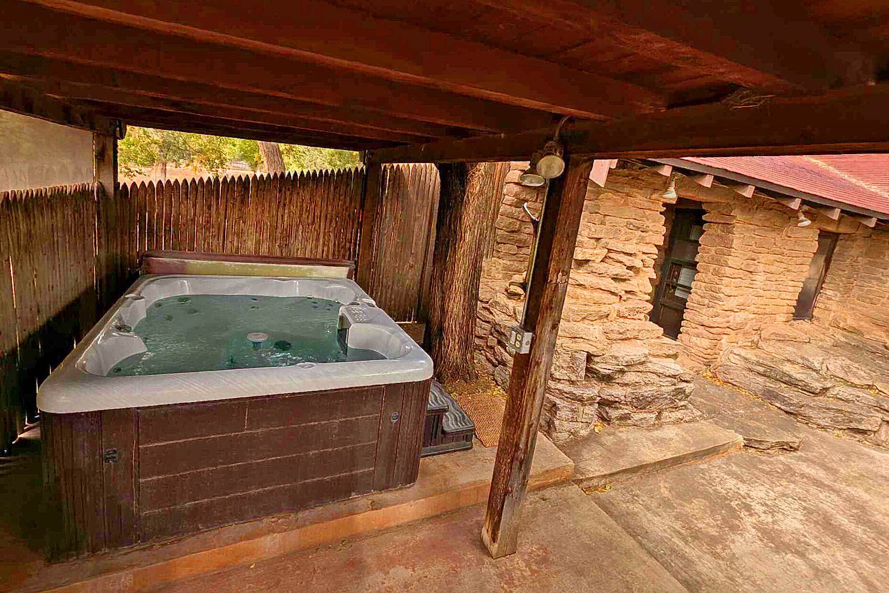 A hot tub is sitting under a wooden roof in front of a stone building.