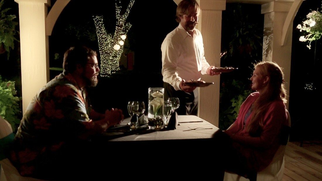 A man is serving a plate of food to a group of people sitting at a table.