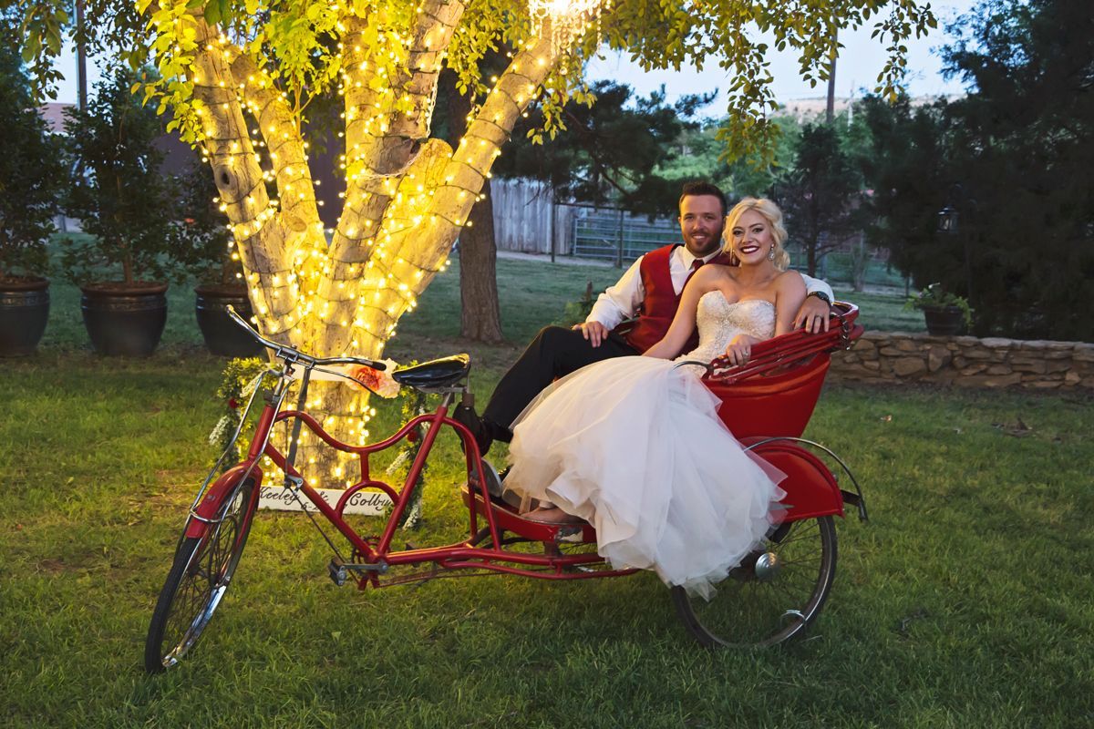 A bride and groom are sitting in a red bicycle.