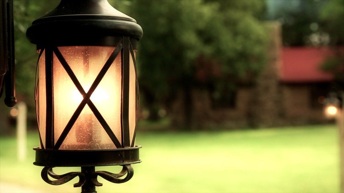 A lantern is lit up in a park with a house in the background.
