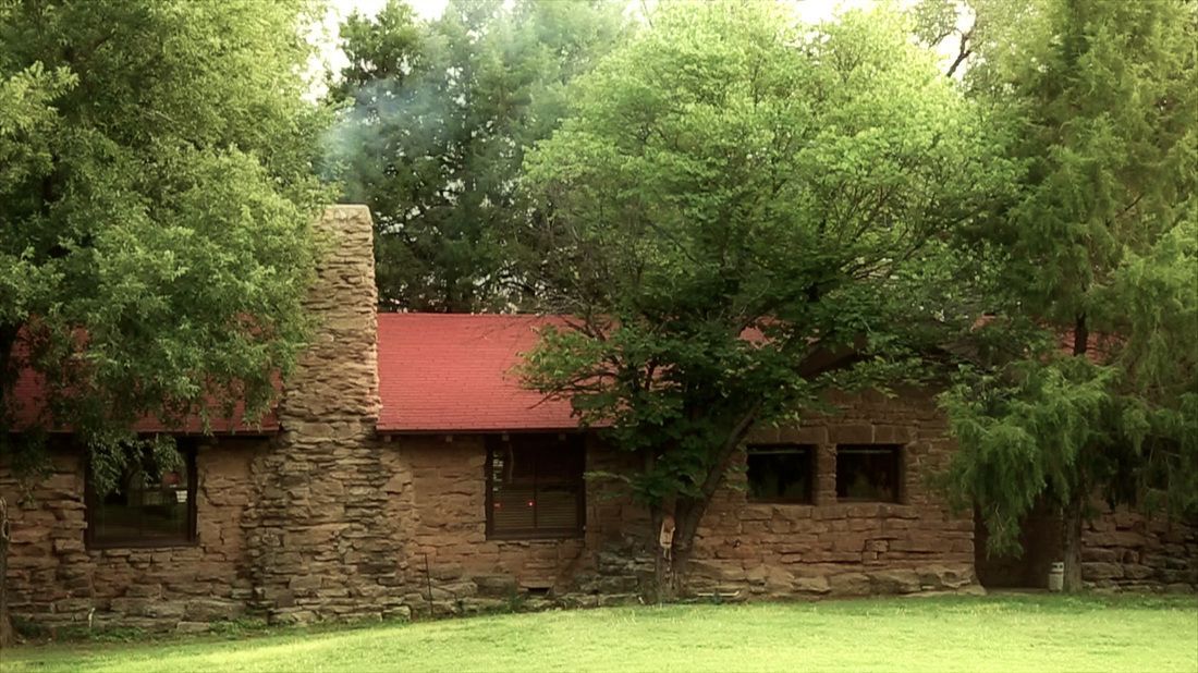 A stone house with a red roof is surrounded by trees.