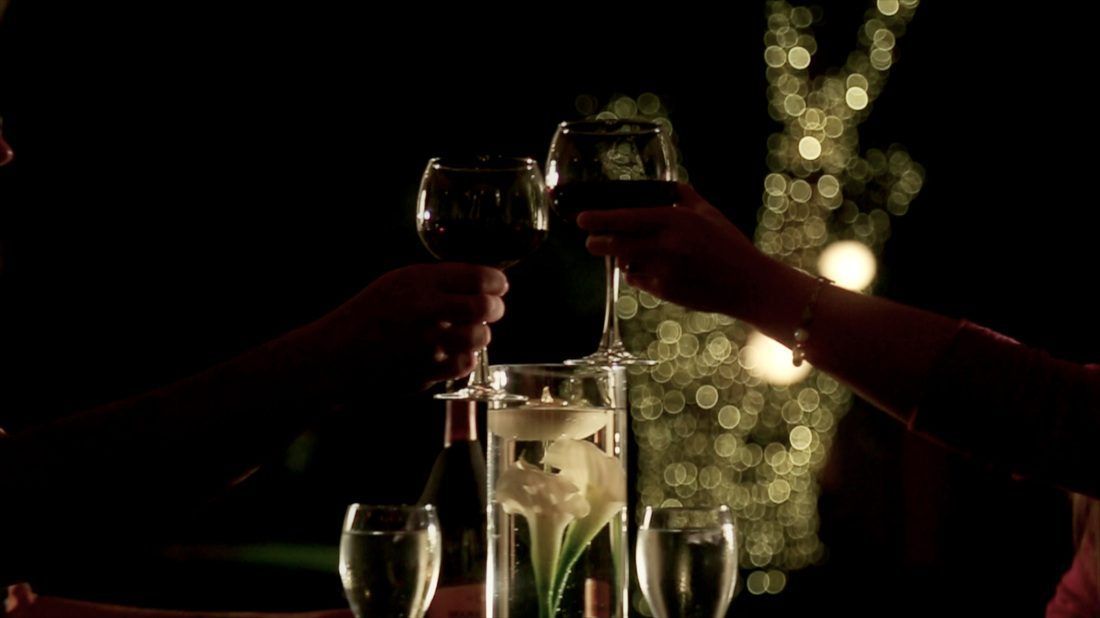 Two people are toasting with wine glasses at a table.