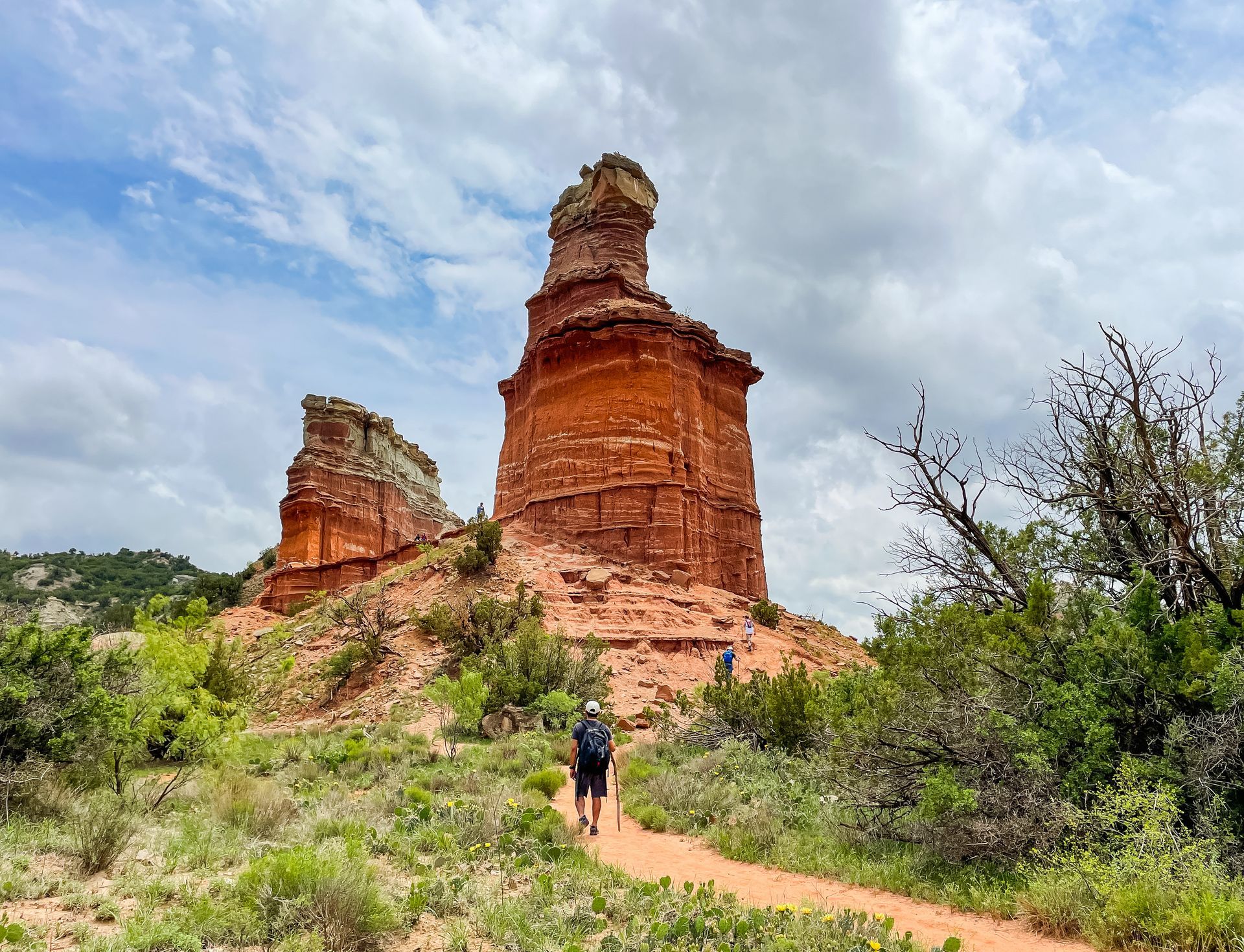 A group of people are walking down a dirt path towards a large rock formation.