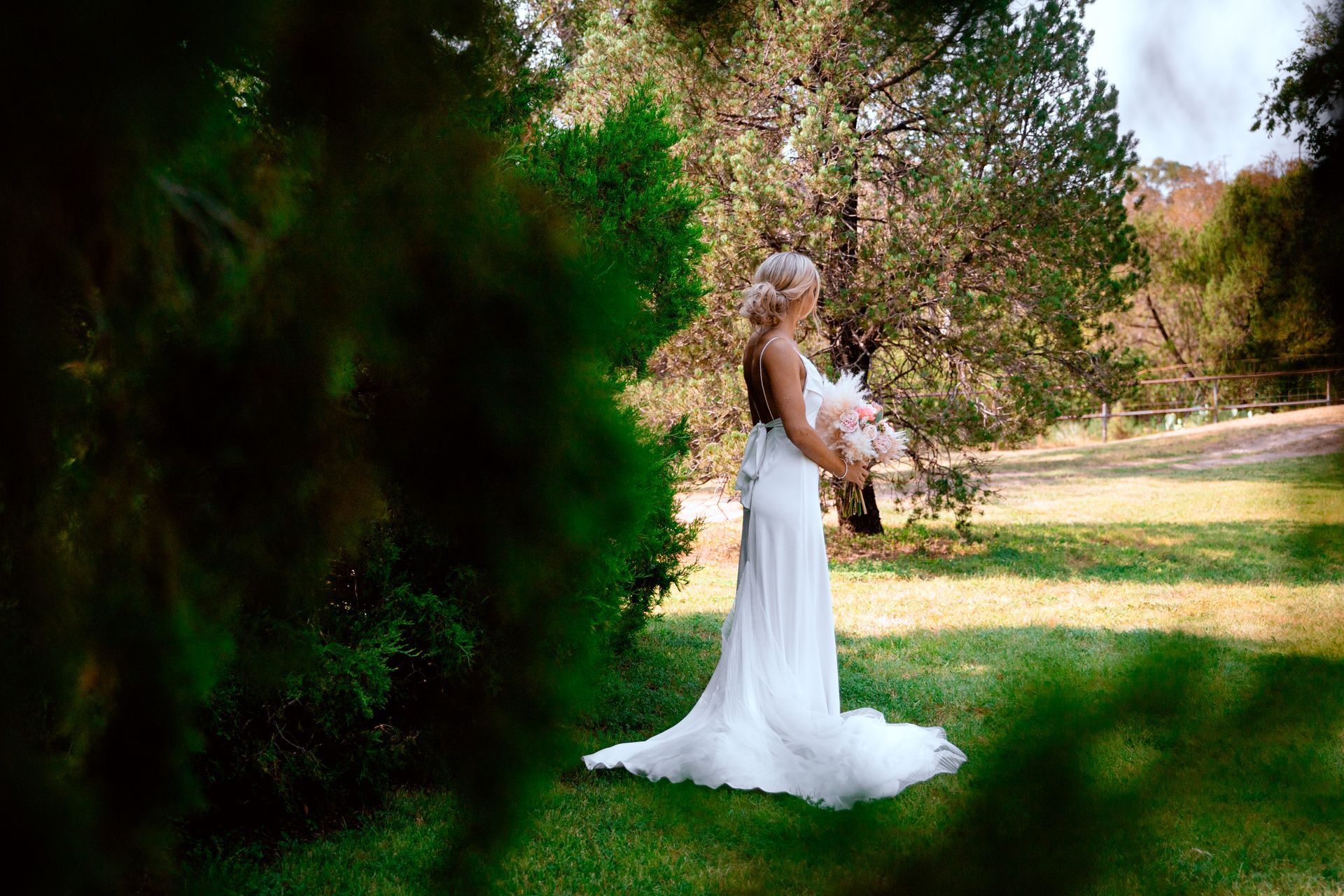 A bride in a white dress is standing in the grass holding a bouquet of flowers.