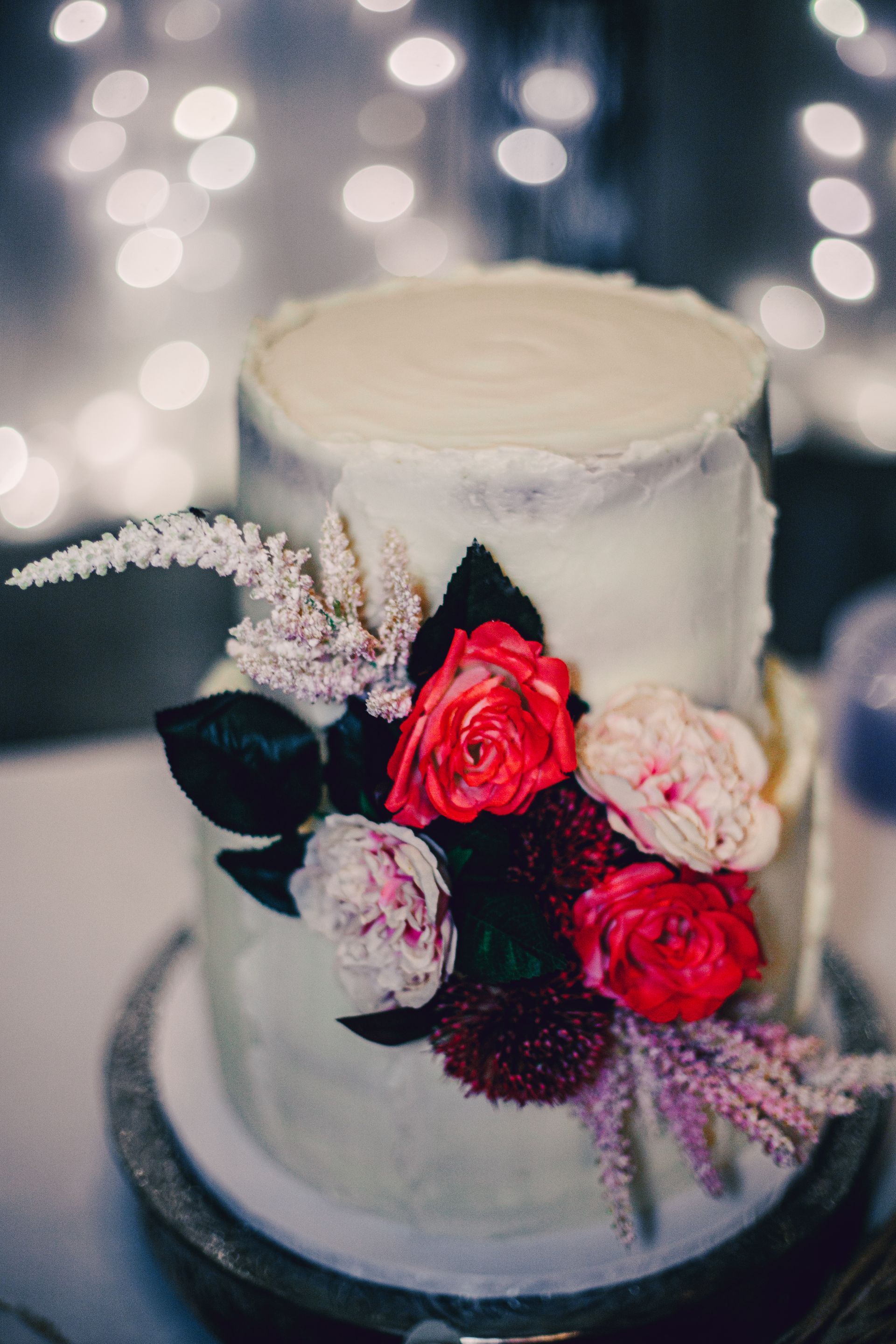 A wedding cake with red and pink flowers on top of it.