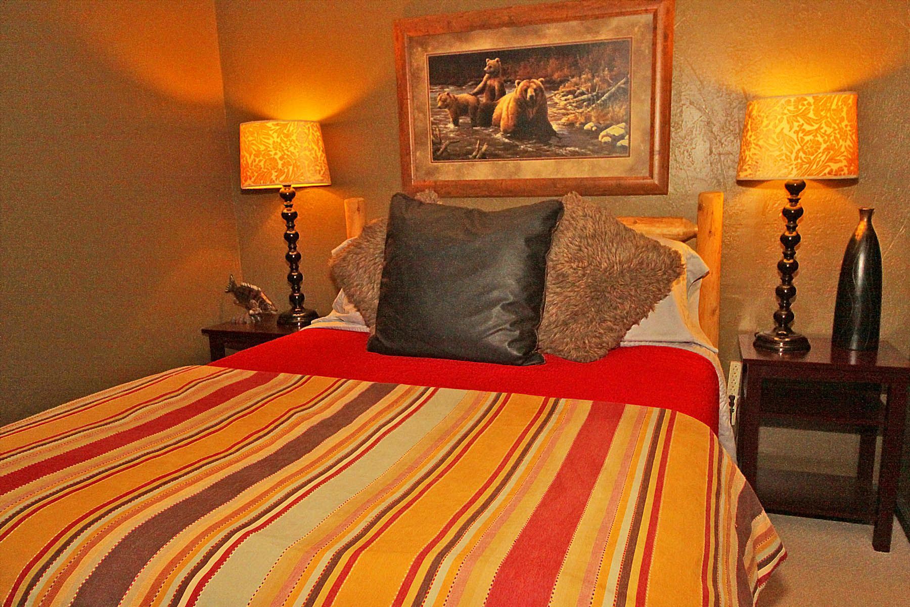 A bedroom with a bed , two lamps and a painting on the wall