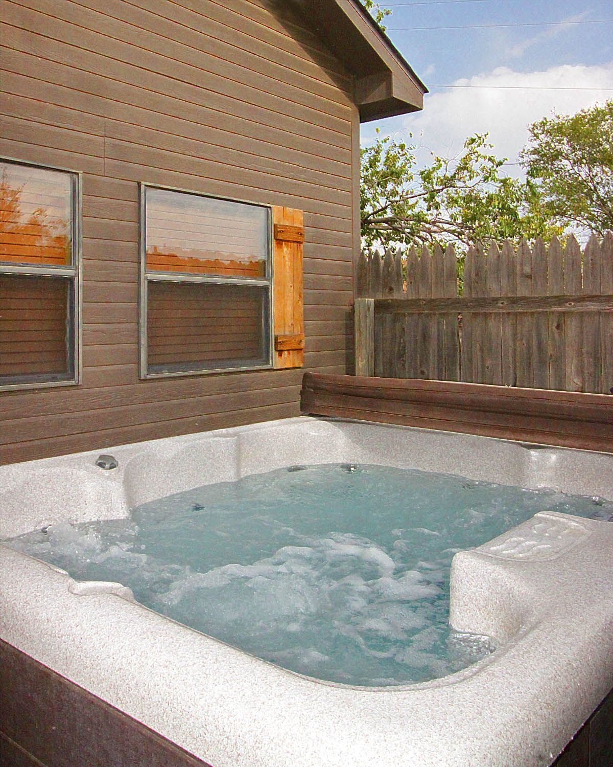 A hot tub is sitting outside of a house next to a wooden fence.