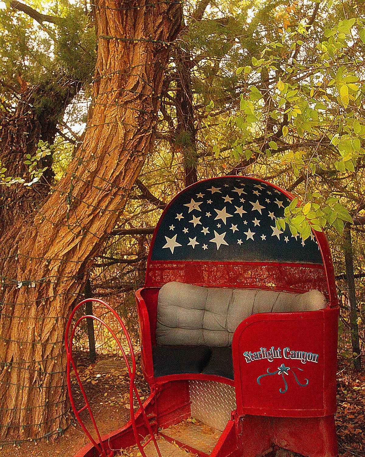 A red mailbox with an american flag design sits under a tree