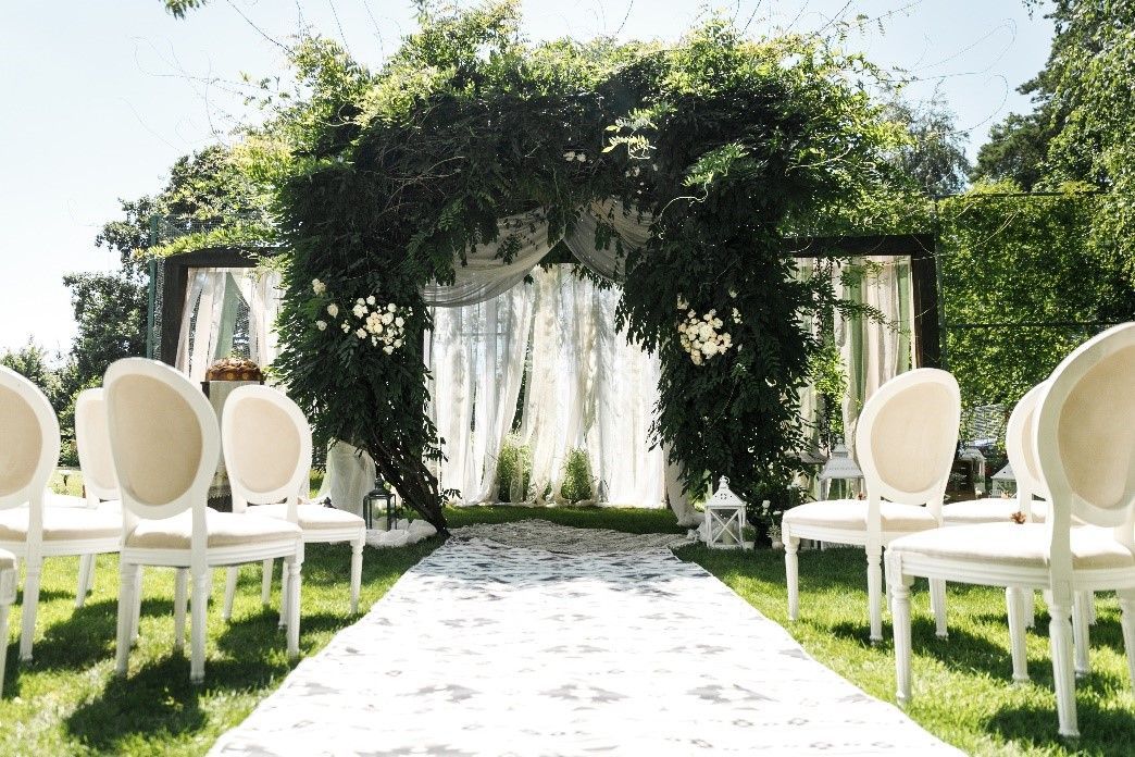 A row of white chairs are lined up in front of a wedding arch.