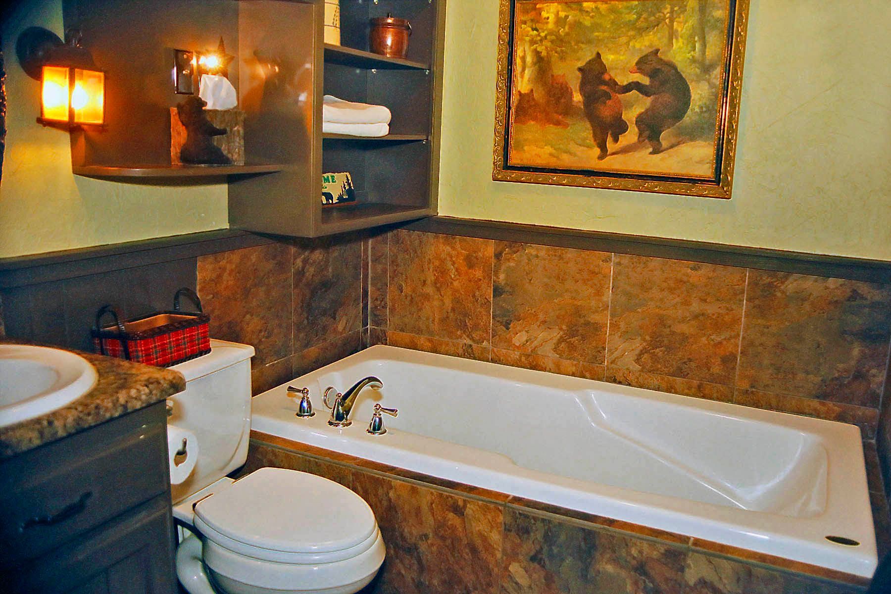 A bathroom with a tub , toilet , sink and a painting of two bears on the wall.