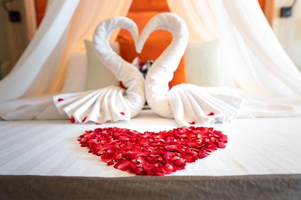 A bed with two swans made out of towels and rose petals