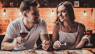 A man and a woman are sitting at a table eating pasta and drinking wine.
