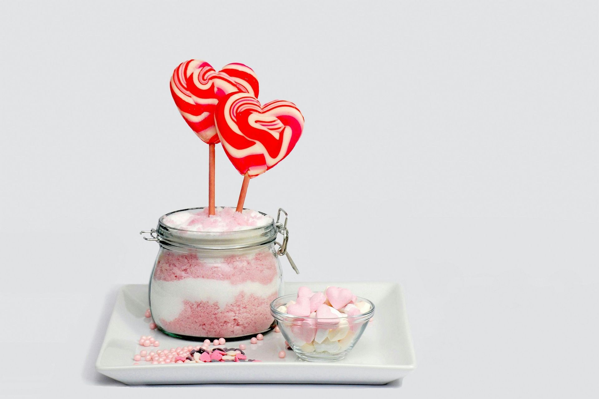 Two heart shaped lollipops are sitting on top of a jar of pink powder.