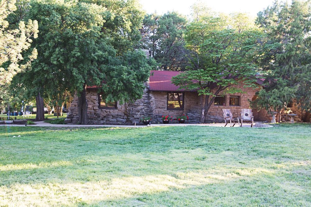 A stone house with a red roof is surrounded by trees and grass.