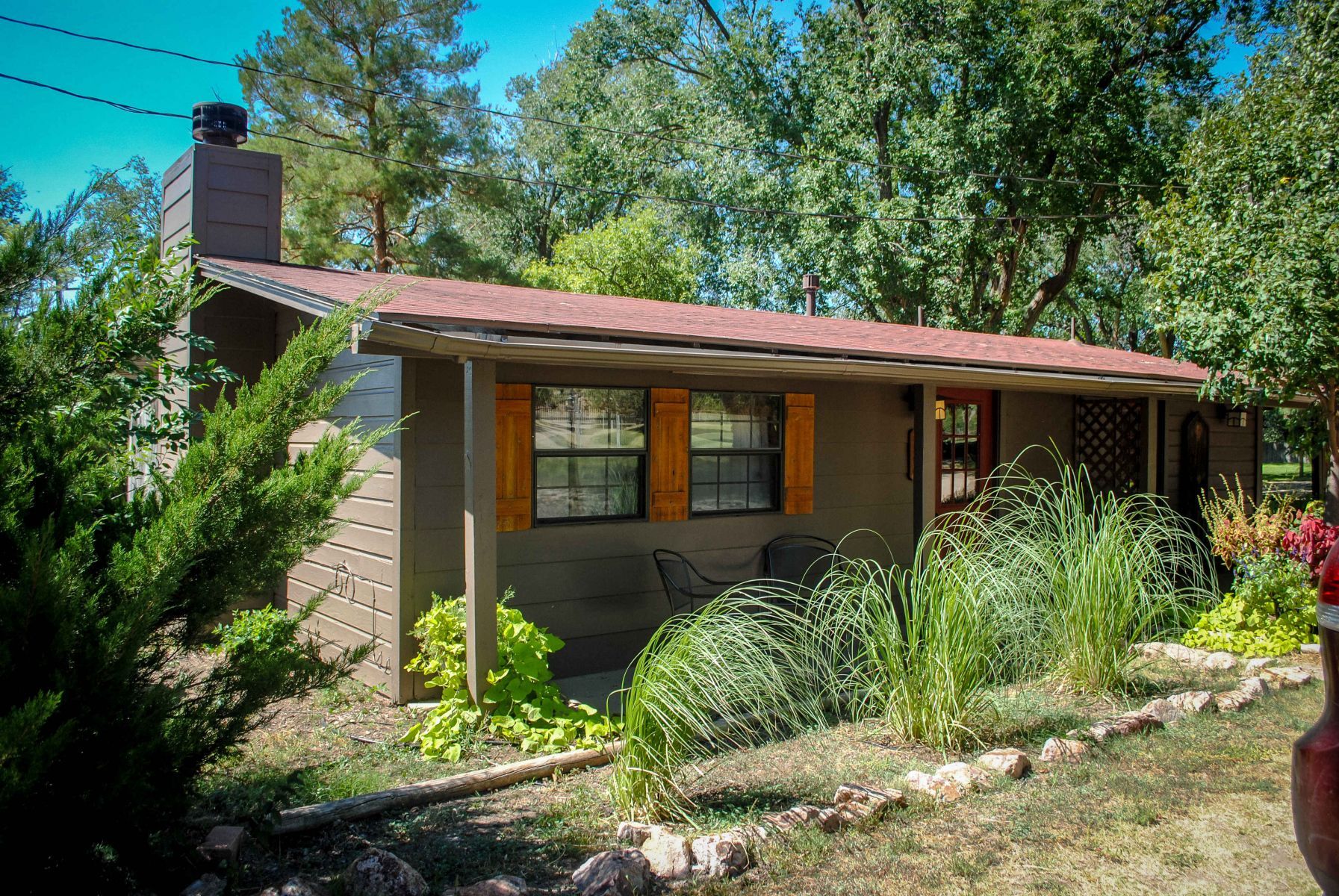 A small house with a red roof is surrounded by trees and bushes.