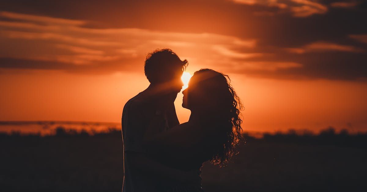 A man and a woman are kissing in front of a sunset.