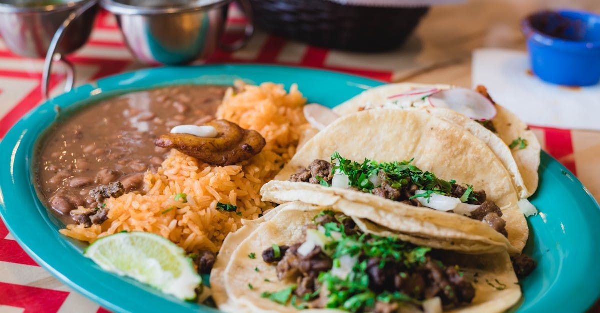 A blue plate topped with tacos , rice and beans on a table.