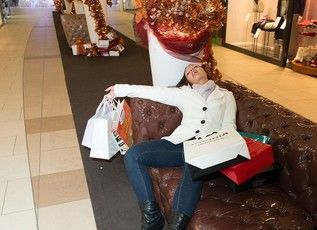 A woman is laying on a couch in a mall holding shopping bags.