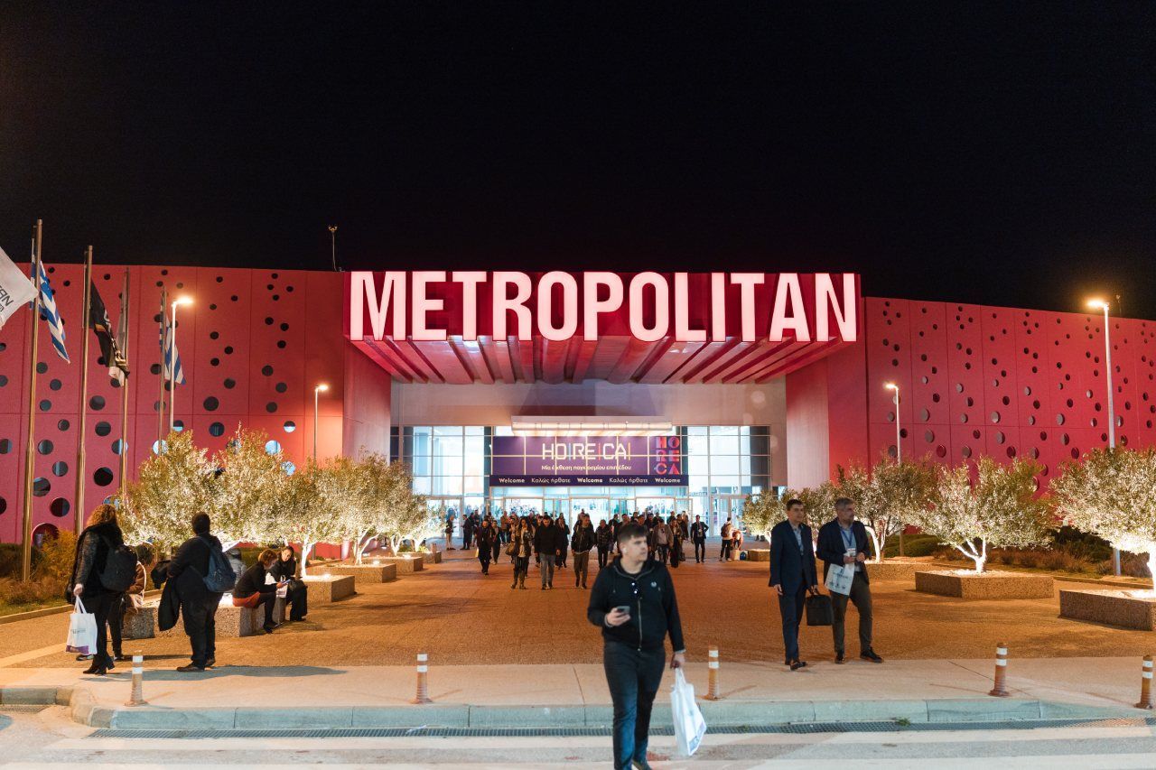 Um grupo de pessoas está caminhando em frente a um grande prédio vermelho que diz metropolitan.