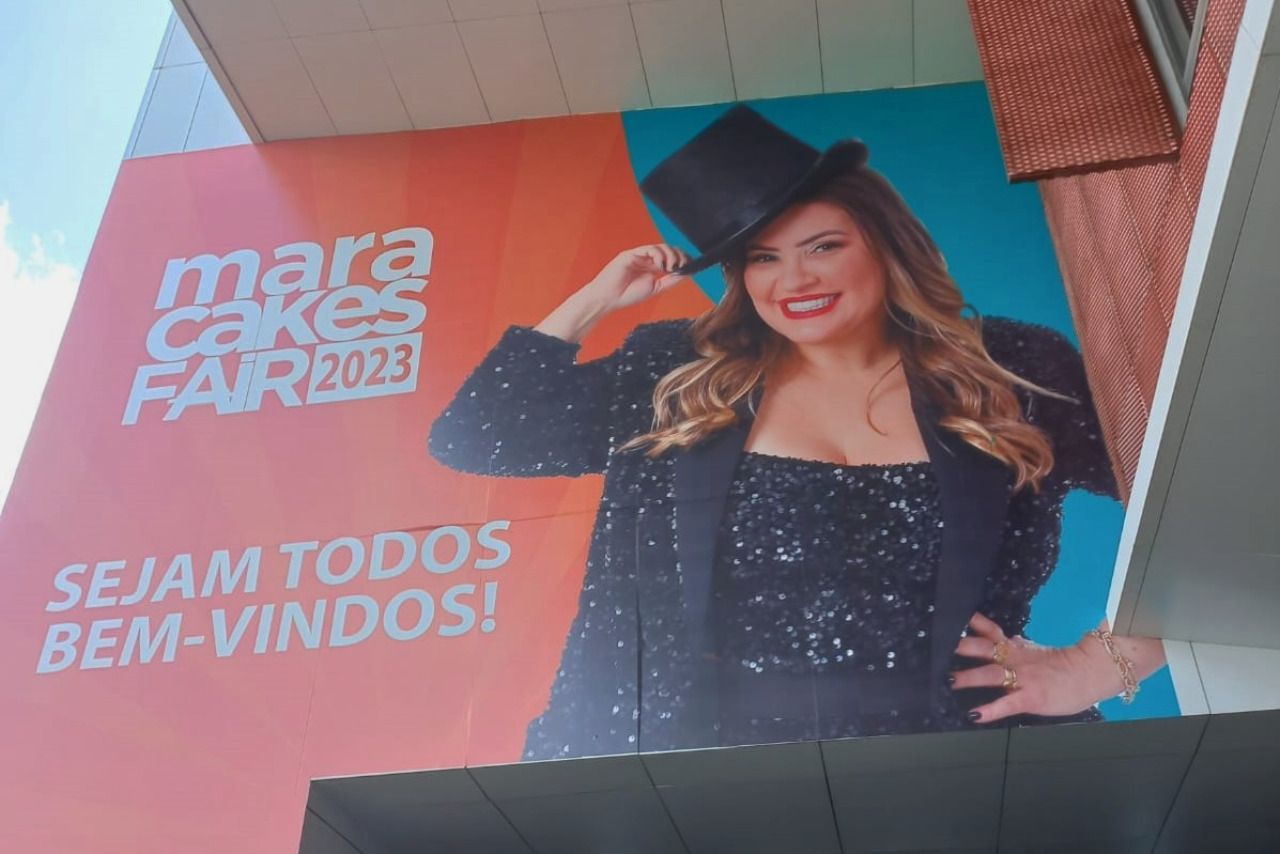 Uma mulher usando uma cartola está em um outdoor da feira de bolos Mara