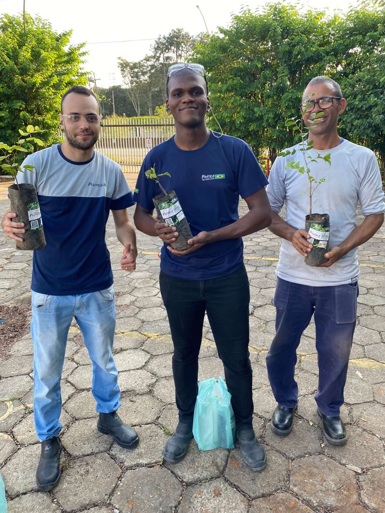 Três homens estão de pé, um ao lado do outro, segurando vasos de plantas.