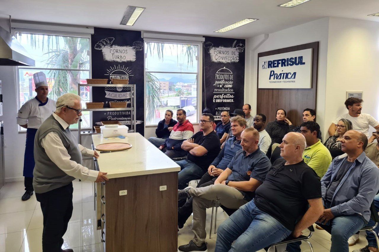 Um homem está de pé na frente de um grupo de pessoas sentadas em cadeiras.