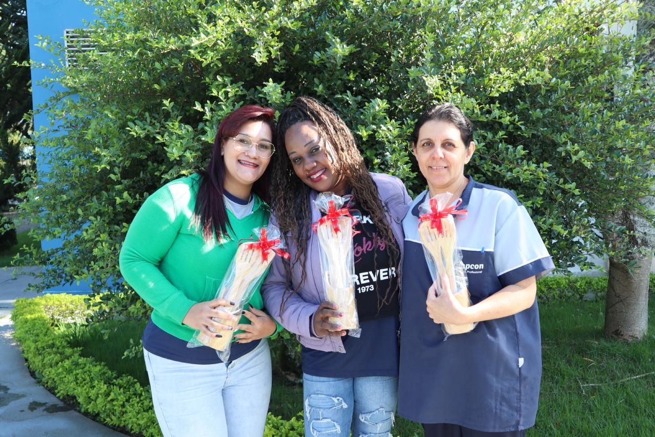 Três mulheres estão de pé, uma ao lado da outra, segurando buquês de flores.